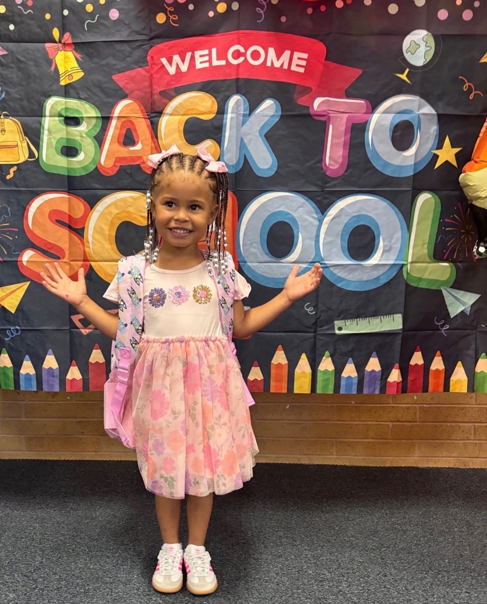Child smiling in front of a welcome back to school banner